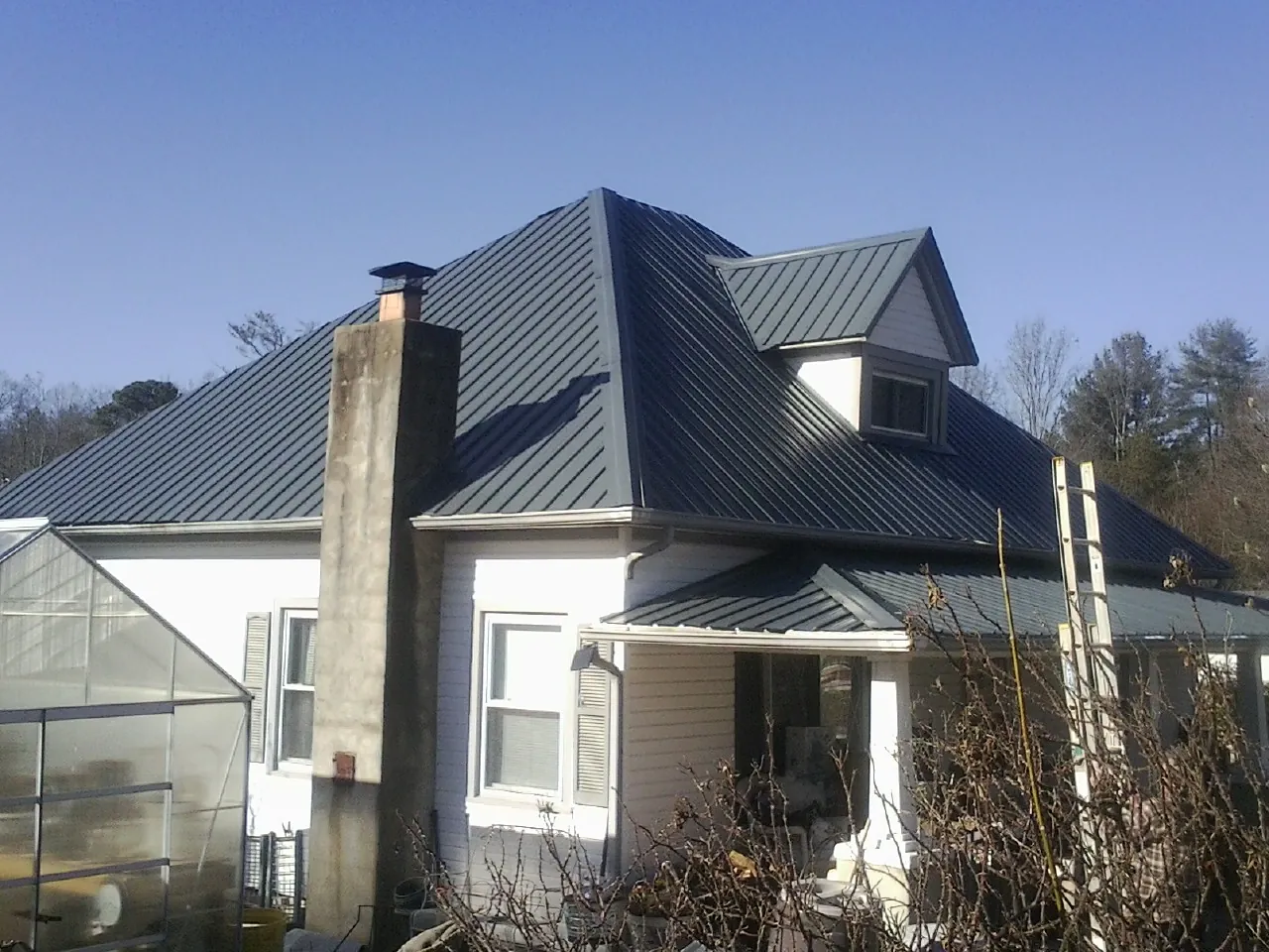 Dark blue standing seam metal roof on a white farmhouse with dormer — Slate & Tile Roof Repair by Roofing Brothers in Belleair Beach