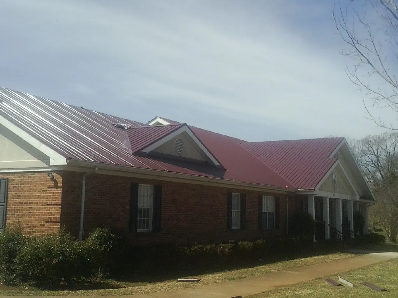 Red metal roof with gabled entries on a long brick building, from a Hail Damage Roof Repair job in Belleair Beach