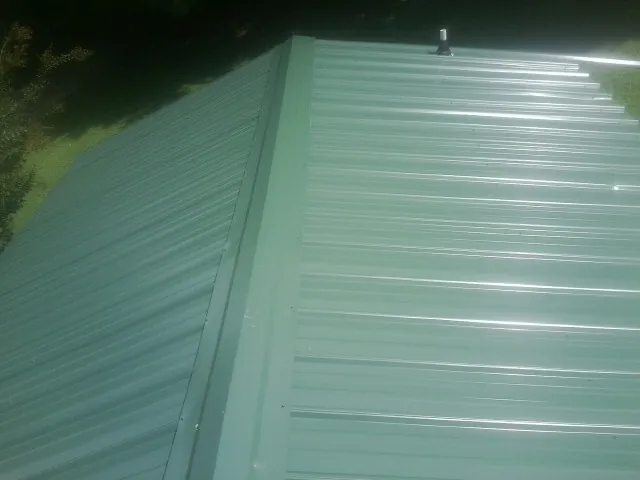New green metal panels meeting at the ridge of a roof — Flat Roof Repair work by our crew in Belleair Beach