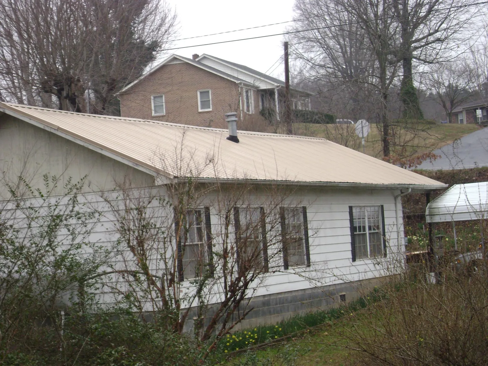 Tan metal roof on a white sided house set into a hillside — Commercial Roofing by Roofing Brothers in Belleair Beach