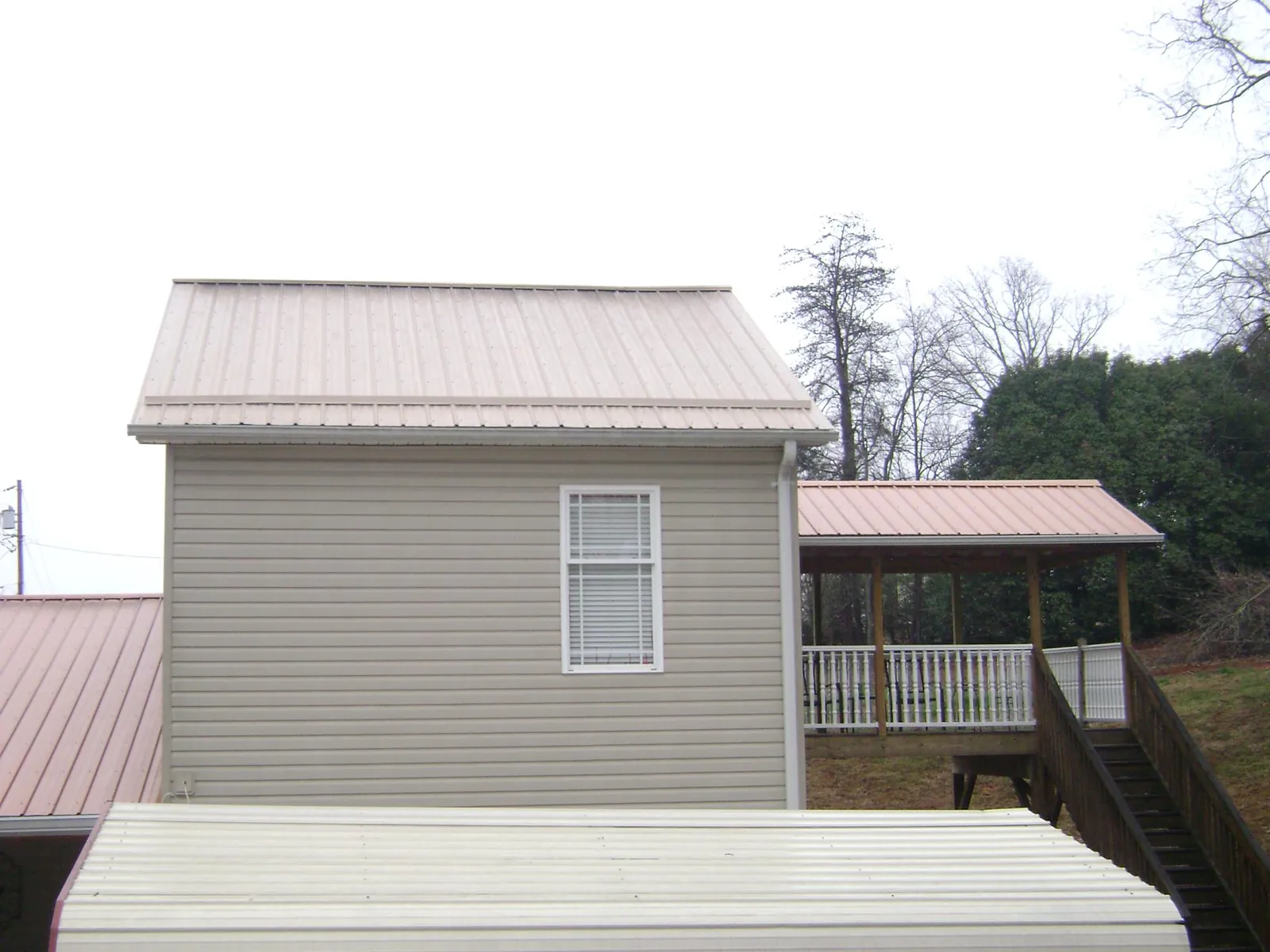 Tan metal roofs on a two story addition and attached porch, from a Roof Replacement job in Belleair Beach